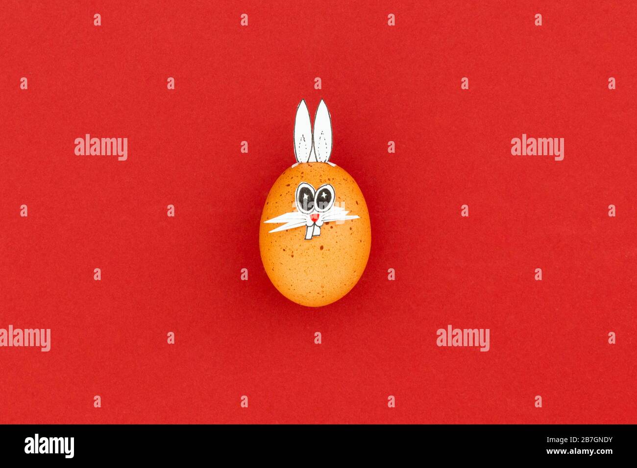 Brown easter egg with funny bunny ears and cartoon face on red background Stock Photo