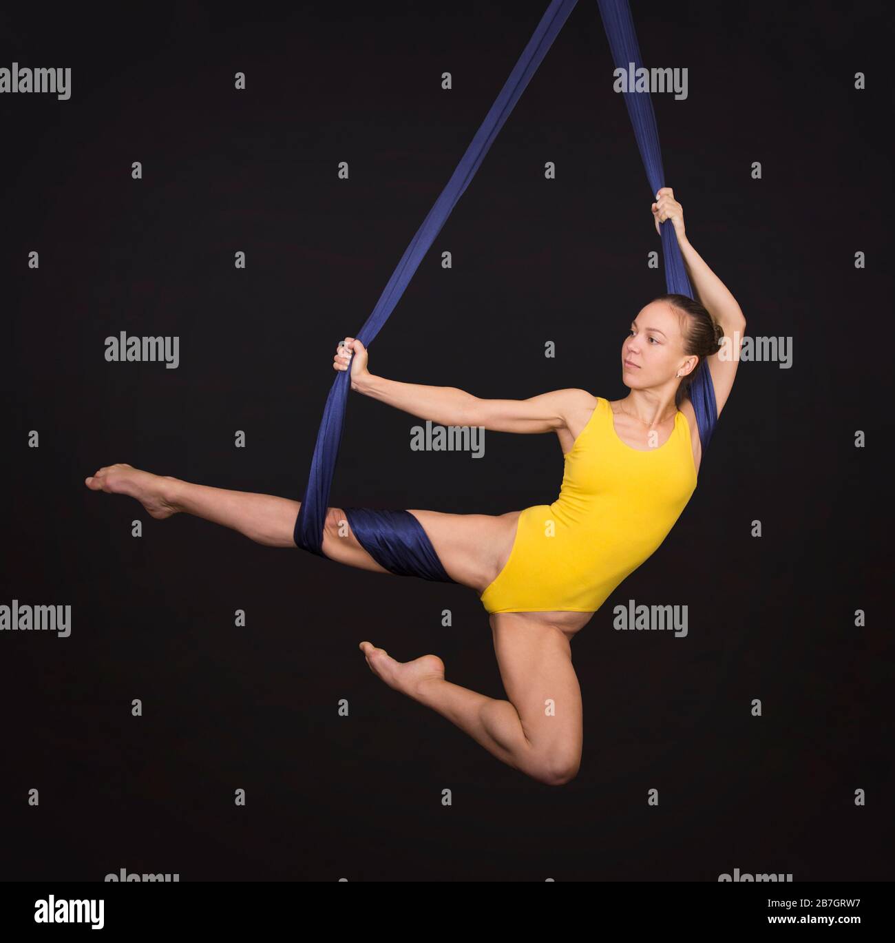 Young, smiling woman doing exercises on aerial silk. Studio shooting on a dark background. Stock Photo