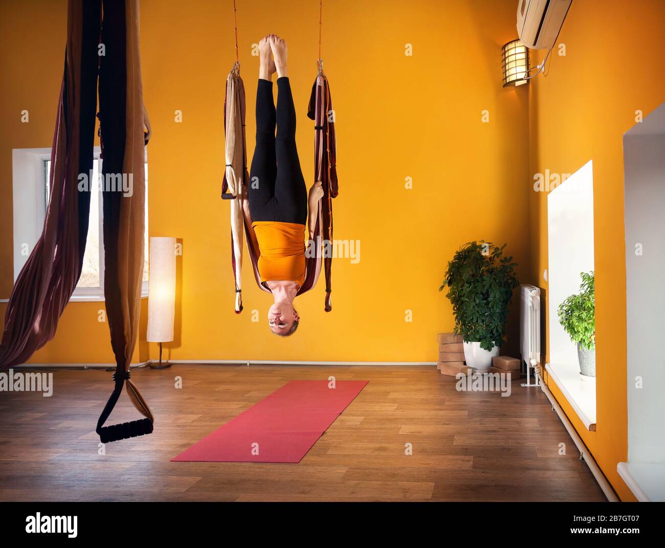 Young woman doing antigravity yoga upside down position in fitness club