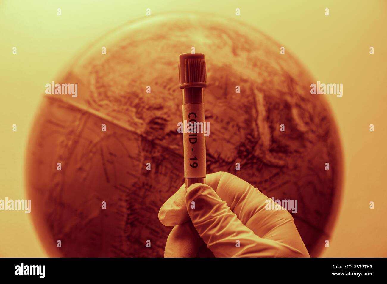 concept of world infected by the coronavirus (covid-19) with hand wearing a glove and holding a infected sample tube Stock Photo