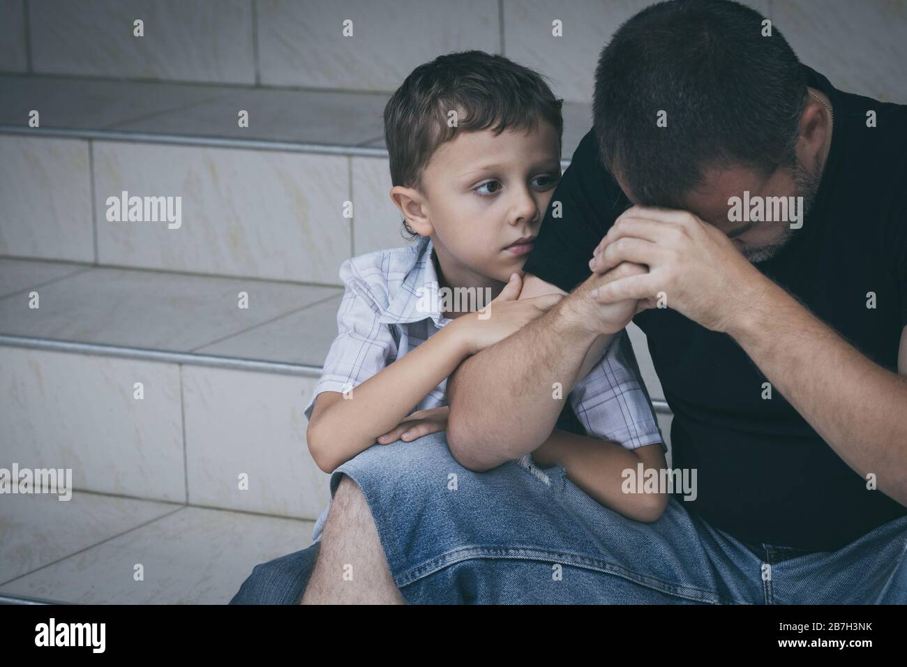 Portrait of young sad little boy and father sitting outdoors at the day ...