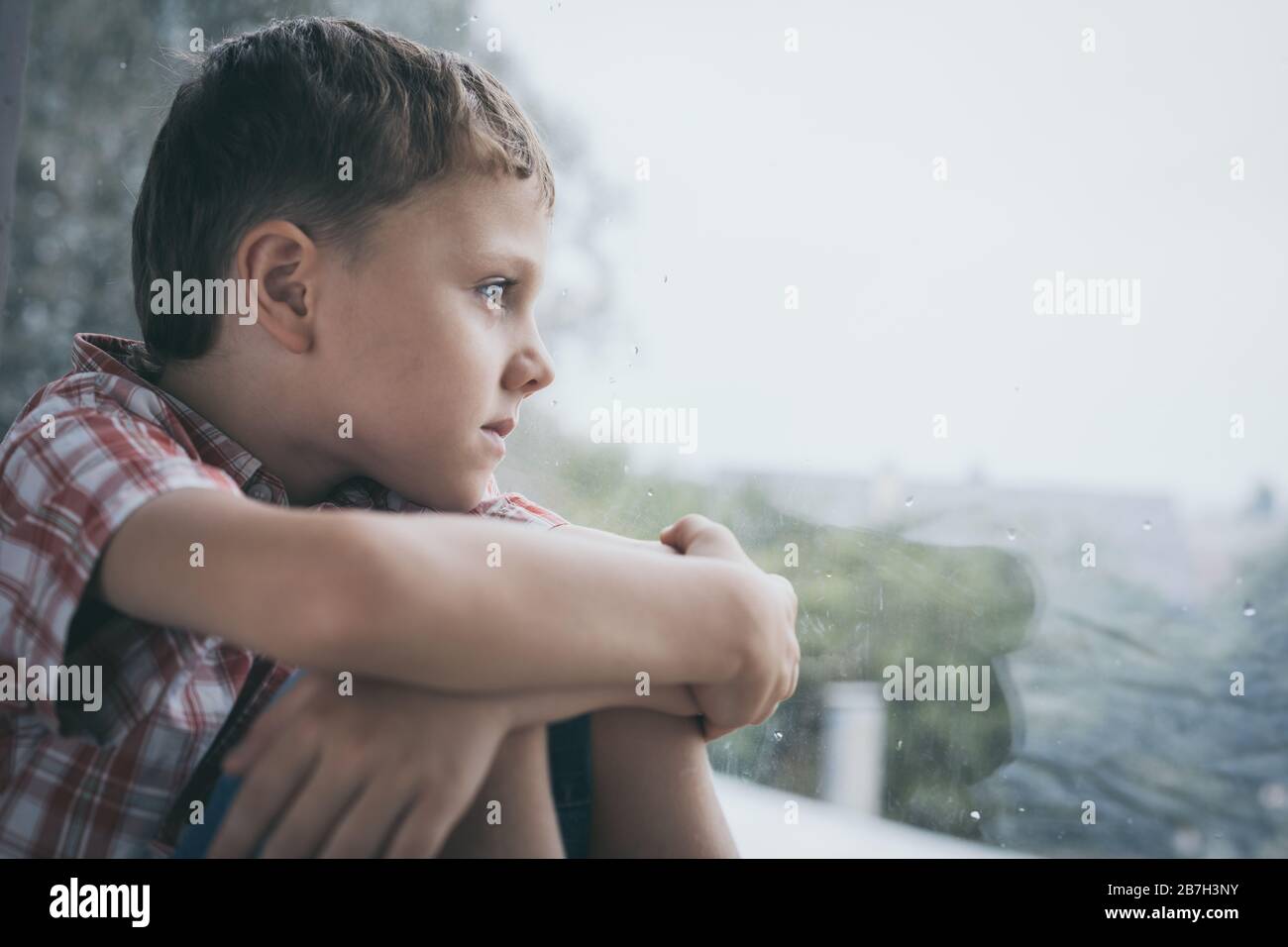 portrait one sad little boy sitting near a window at the day time. Stock Photo