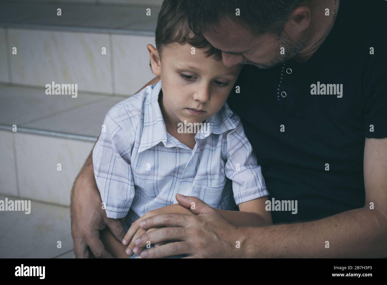 Portrait of young sad little boy and father sitting outdoors at the day time. Concept of sorrow. Stock Photo