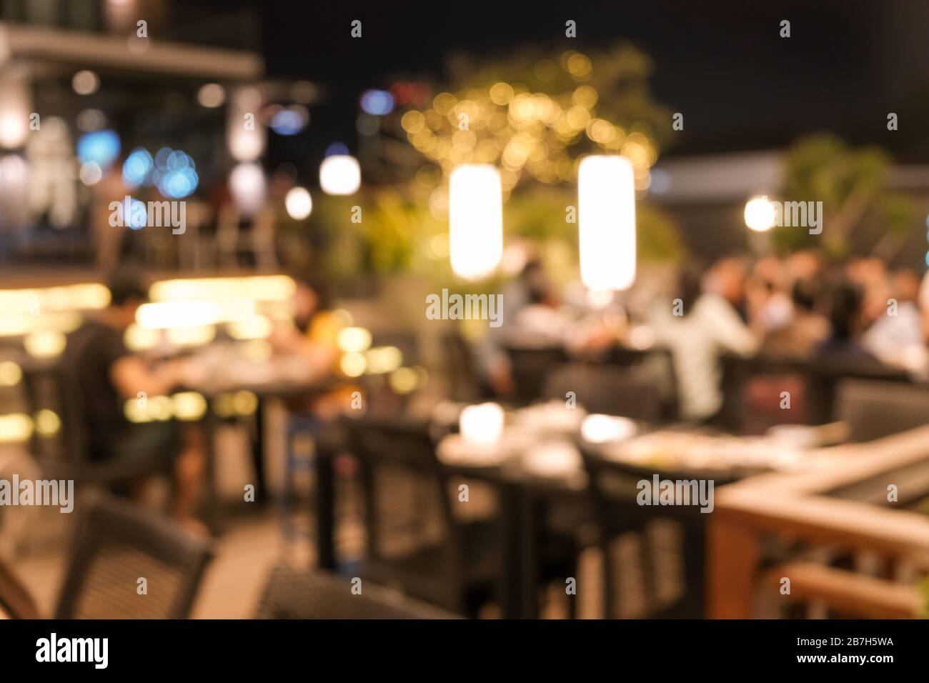 Abstract blur outdoor restaurant interior as background. Tables and chairs and beatiful vintage warm light bulb. Stock Photo