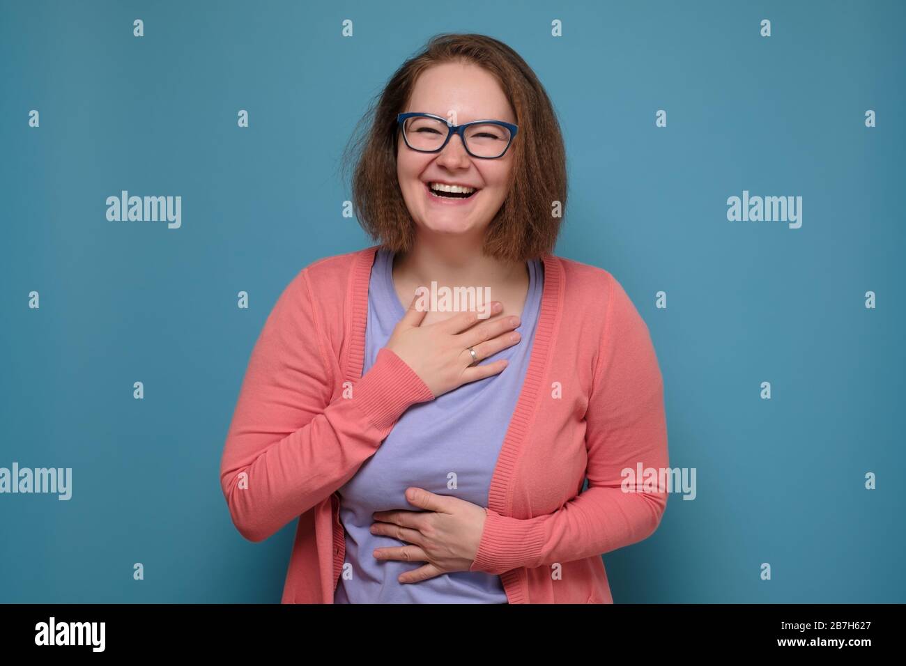 Gorgeous mature woman in pink clothes laughing on funny joke having happy positive mood. Studio shot on blue wall Stock Photo