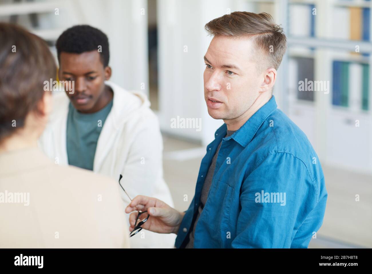 Portrait of adult man sharing life story while sitting on chair in support group circle or psychology center Stock Photo