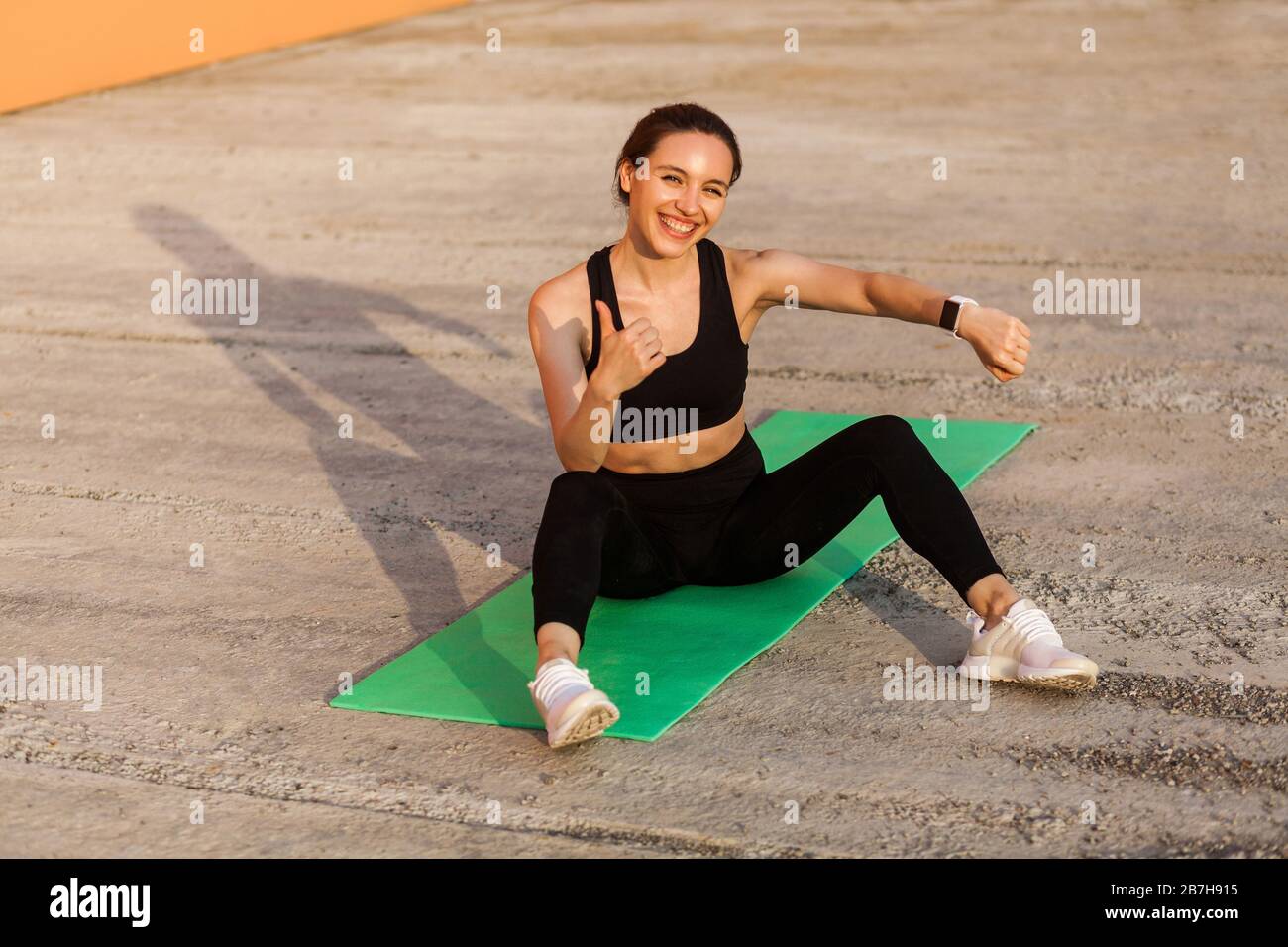 Joyful smiling athletic girl showing wristwatch, fitness tracker on hand, and gesturing thumbs up, satisfied with health indicators after trainings, s Stock Photo