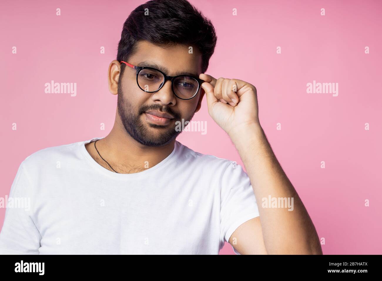 Handsome smart indian guy, student dressed in white t shirt, smiling,  wearing glasses and touching it, posing in studio over pink background.  Facial e Stock Photo - Alamy