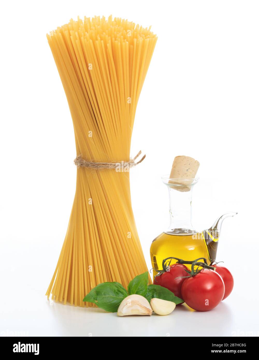 Pasta recipe concept. An uncooked bunch of raw spaghetti pasta, basil, tomatoes, olive oil and garlic on white background. Vertical portrait of tradit Stock Photo