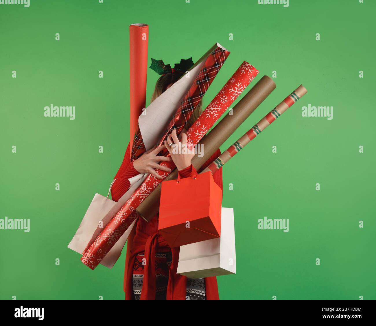 A girl is holding Christmas wrapping paper against a solid green wall and is overwhelmed for a gift supplies idea. Stock Photo
