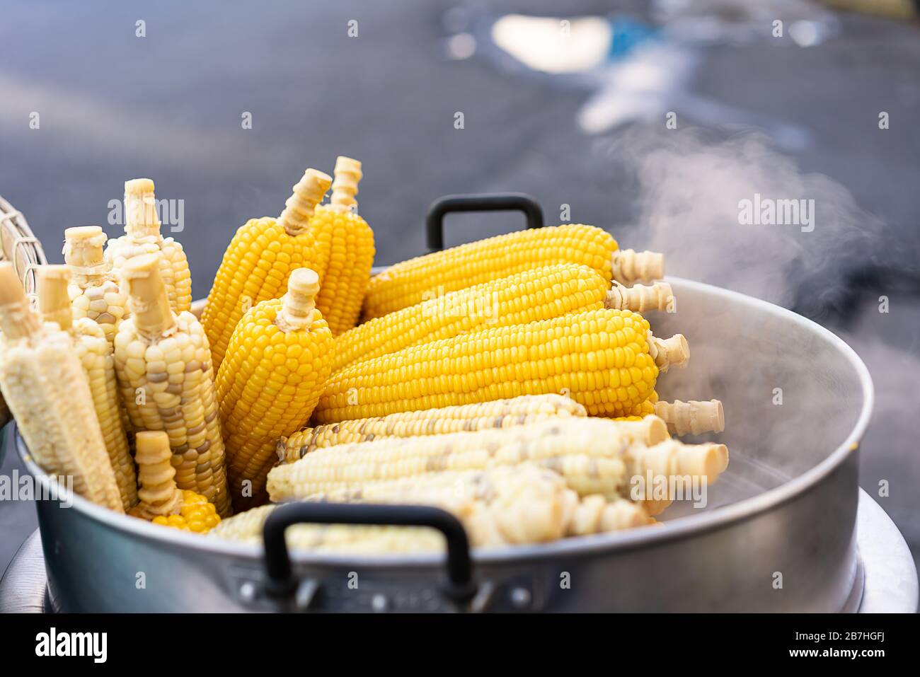 Fresh hot corn on the cob, steaming from the cart of a street food vendor - Freshly cooked corn cobs stacked and for sale at a local hawker market - Delicacy, cuisine and travel foodie concept Stock Photo