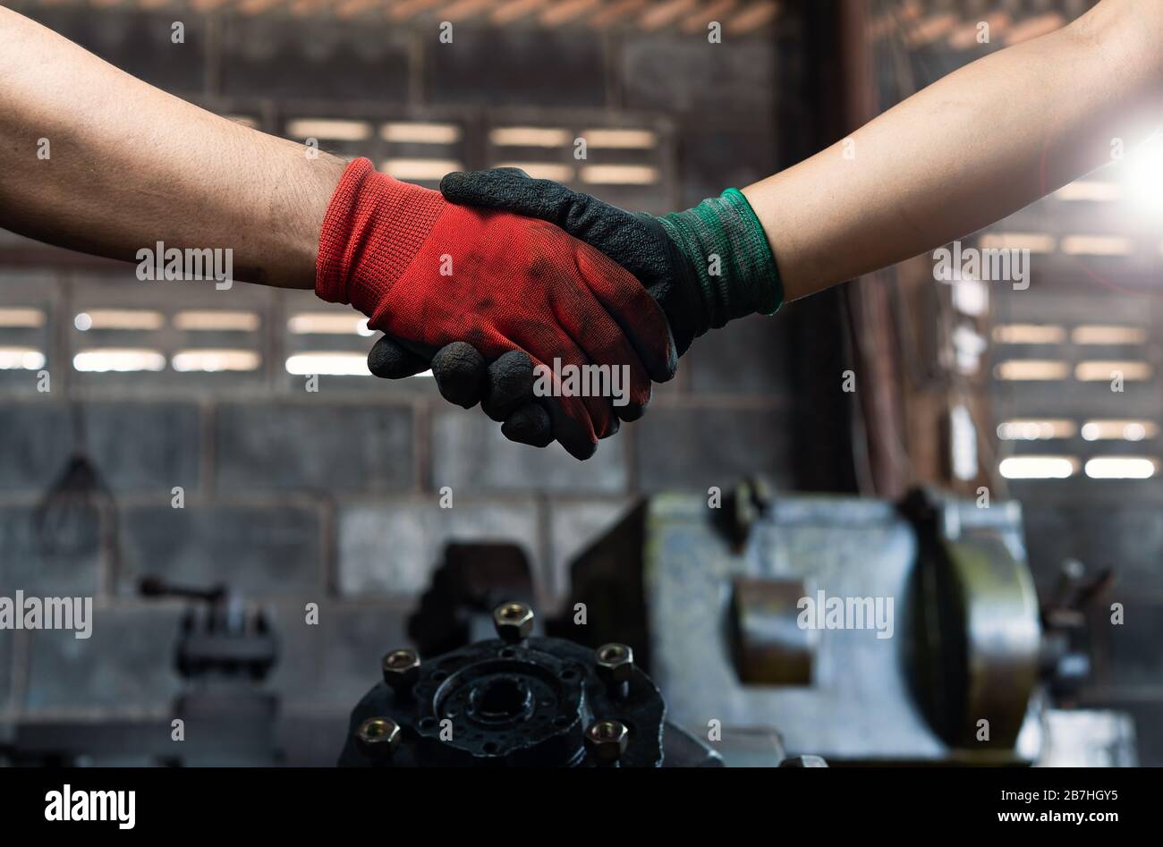 Male and female industrial workers, shaking hands in factory workshop wearing protective workwear - Business and commercial teamwork within the workplace - Working together, goals and success concept Stock Photo
