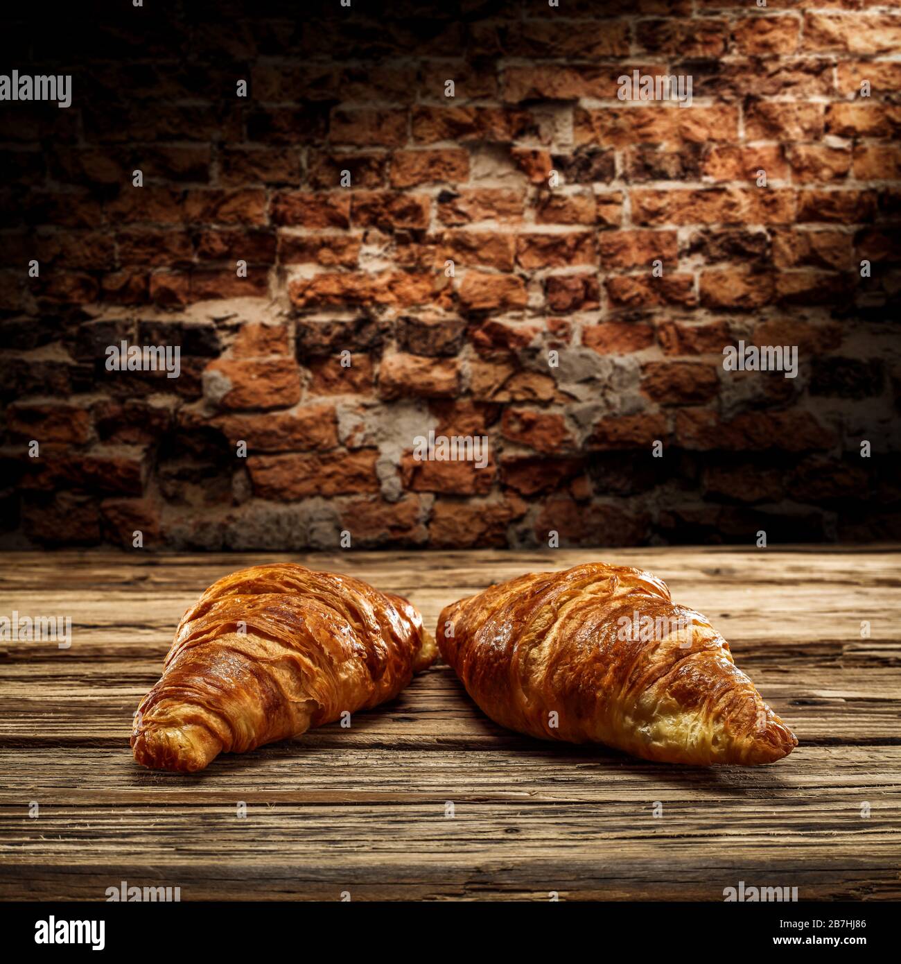 Fresh croissants on desk and free space for your decoration.Dark mood photo of wall with shadows.Copy space for your composition. Stock Photo