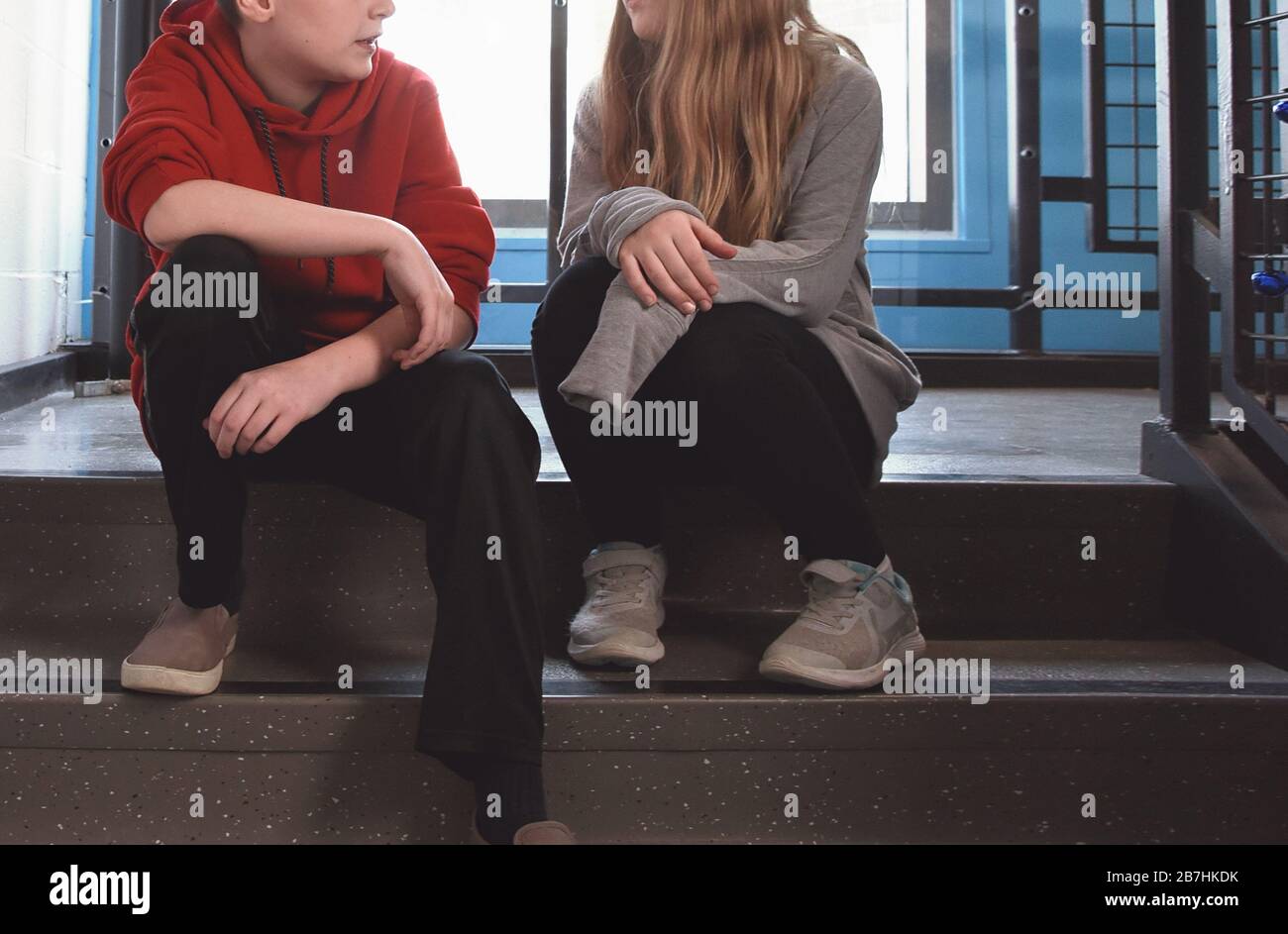 A boy and girl student are sitting in a hallway on stairs talking for a youth communication concept. Stock Photo
