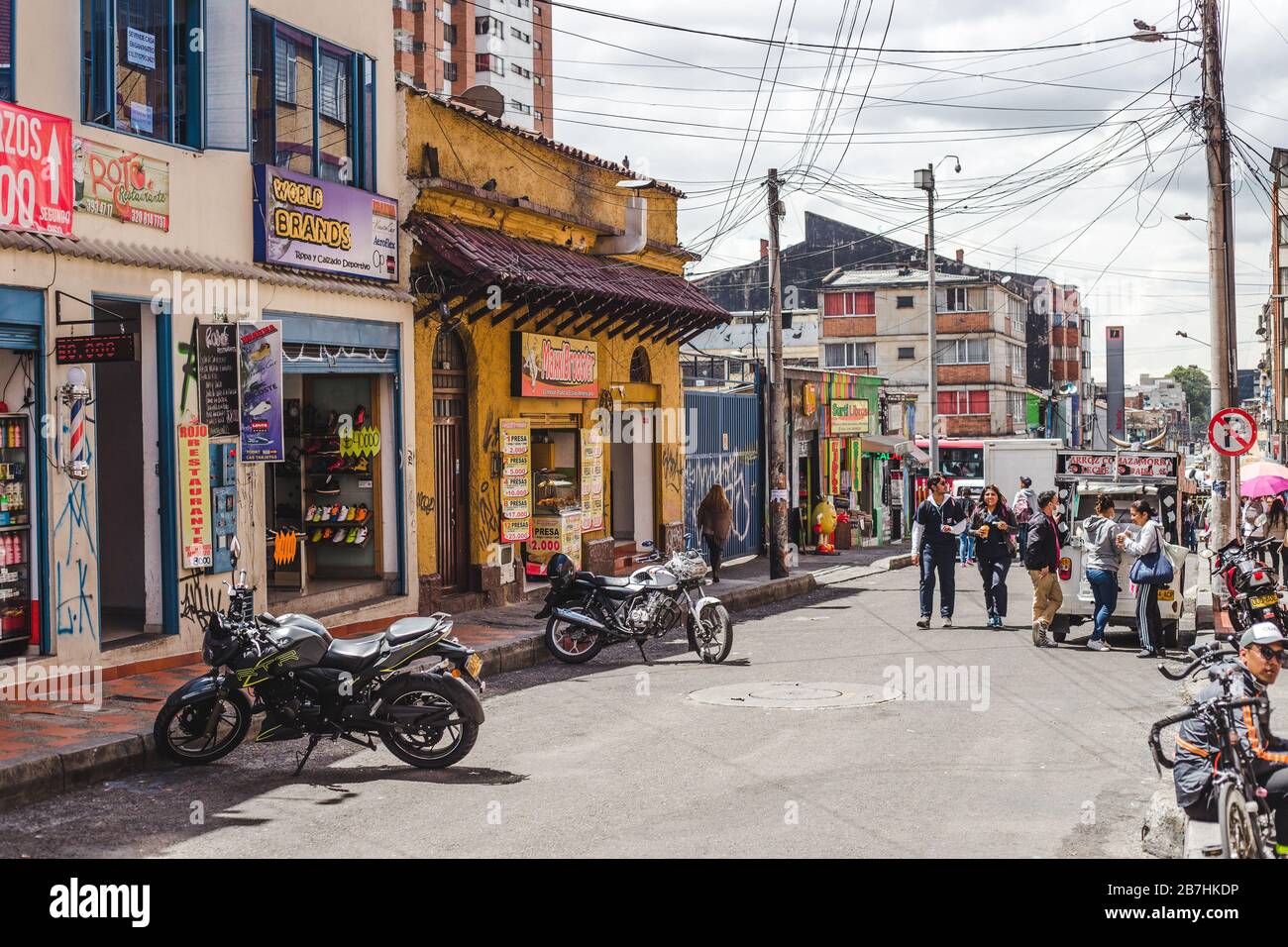 Typical street in Chapinero Central barrio of Bogota, Colombia. Small colorful shopfronts, parked motorbikes and pedestrians buying street food Stock Photo