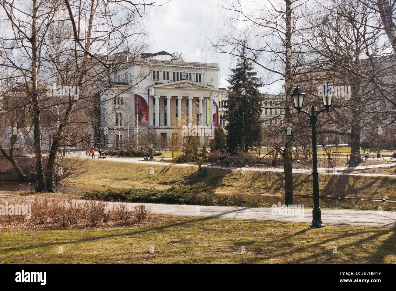 The Latvian National Opera building, built in 1863 in Greek classical style, through the trees as sunshine spills through on a winter afternoon Stock Photo
