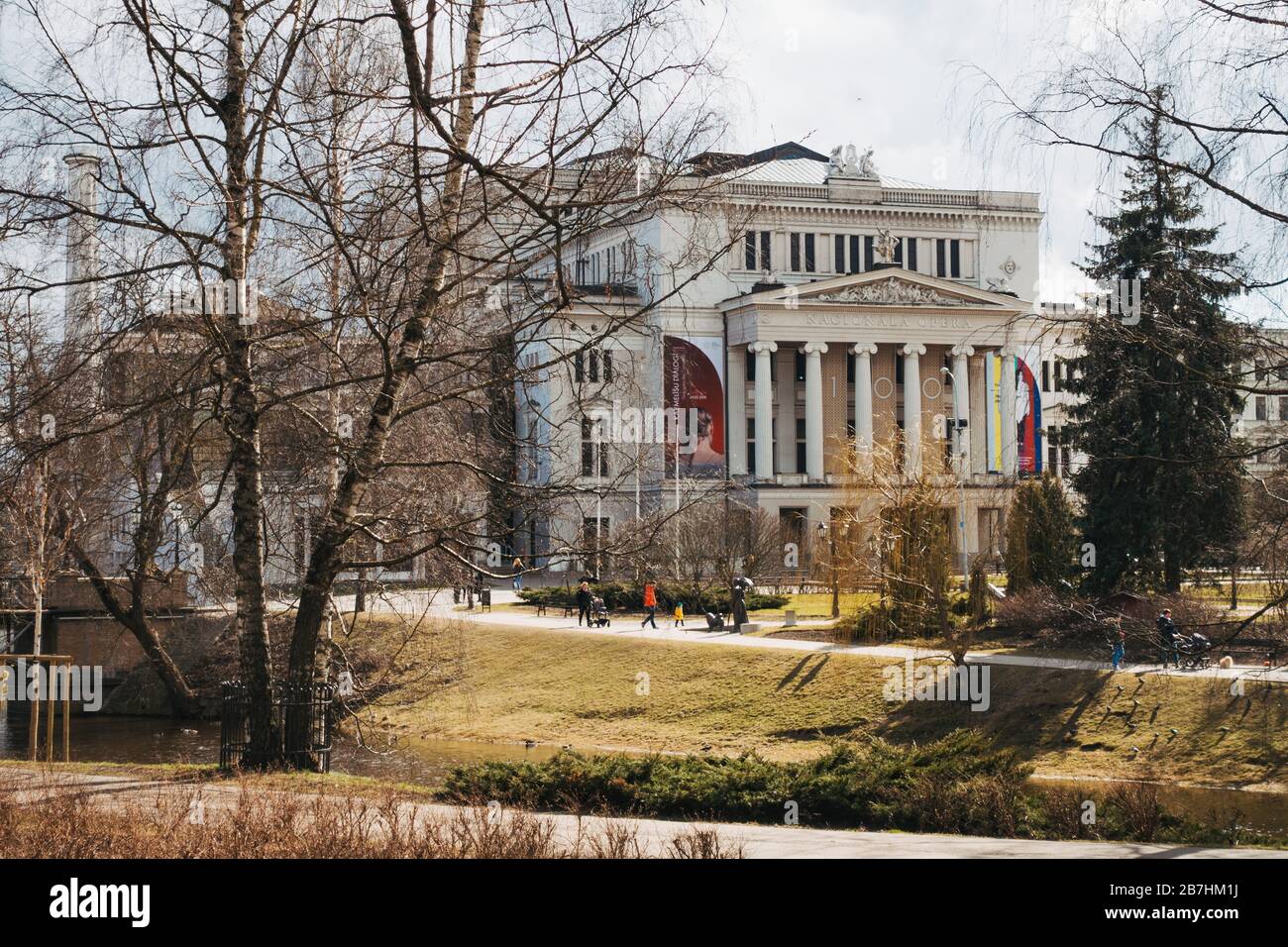 The Latvian National Opera building, built in 1863 in Greek classical style, through the trees as sunshine spills through on a winter afternoon Stock Photo