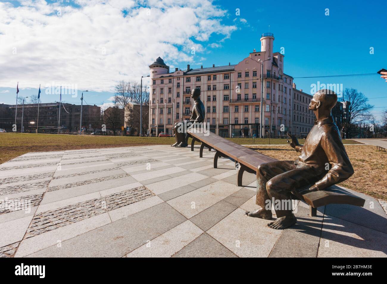 A sculpture of a small and large man on a seat - a play on perspective - in front of the Latvian National Library in Riga, Latvia Stock Photo
