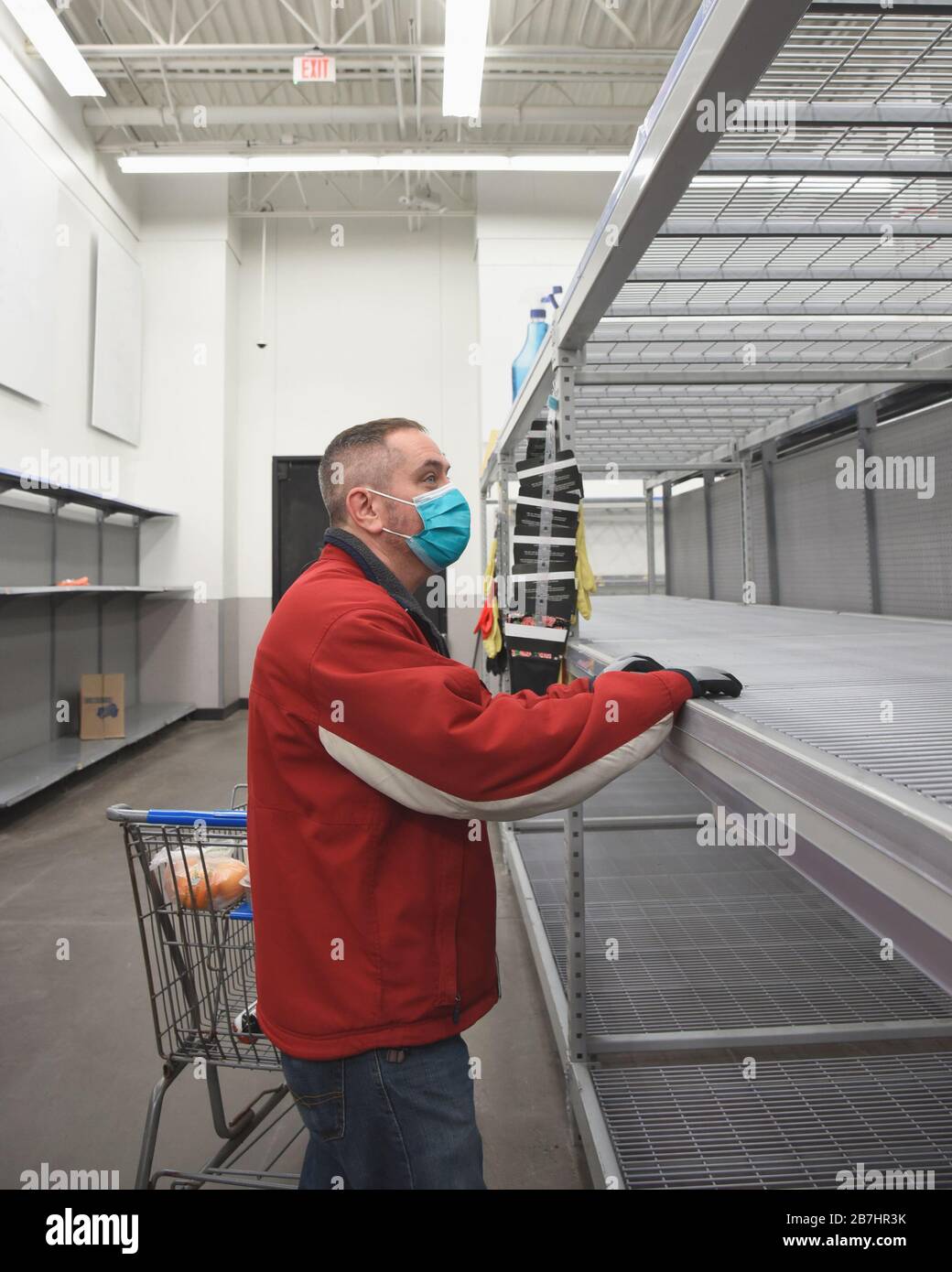 A man is standing in a grocery store wearing a virus mask looking at the empty rack shelf for a corona virus pandemic concept. Stock Photo