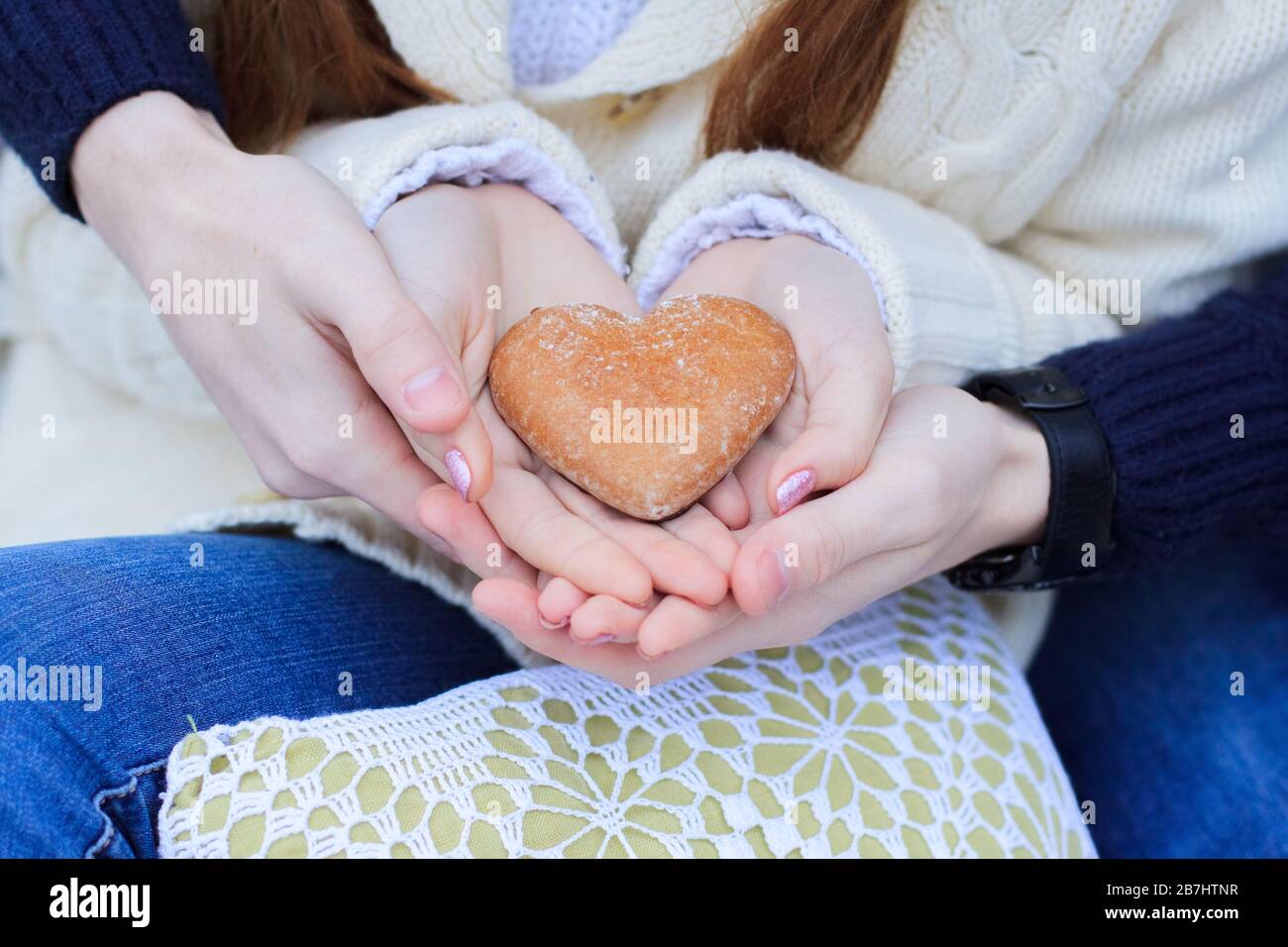 Men's hands hold women's palms in which lies cookies in the form of a heart. A pair in blue jeans holding a gingerbread in the shape of a heart. Close Stock Photo