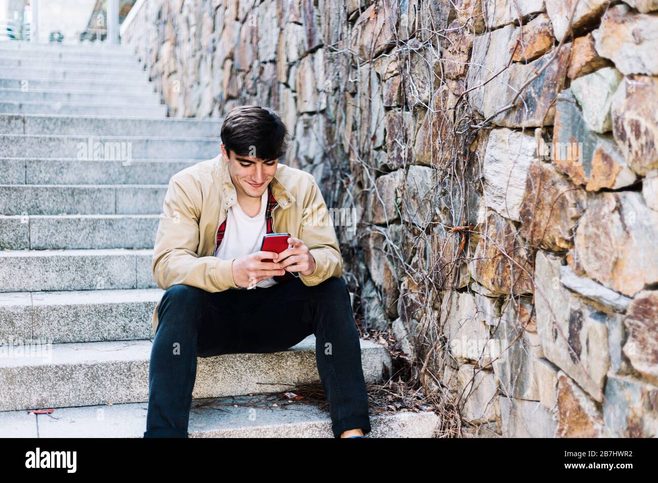Young man using mobile phone while sitting outdoors Stock Photo