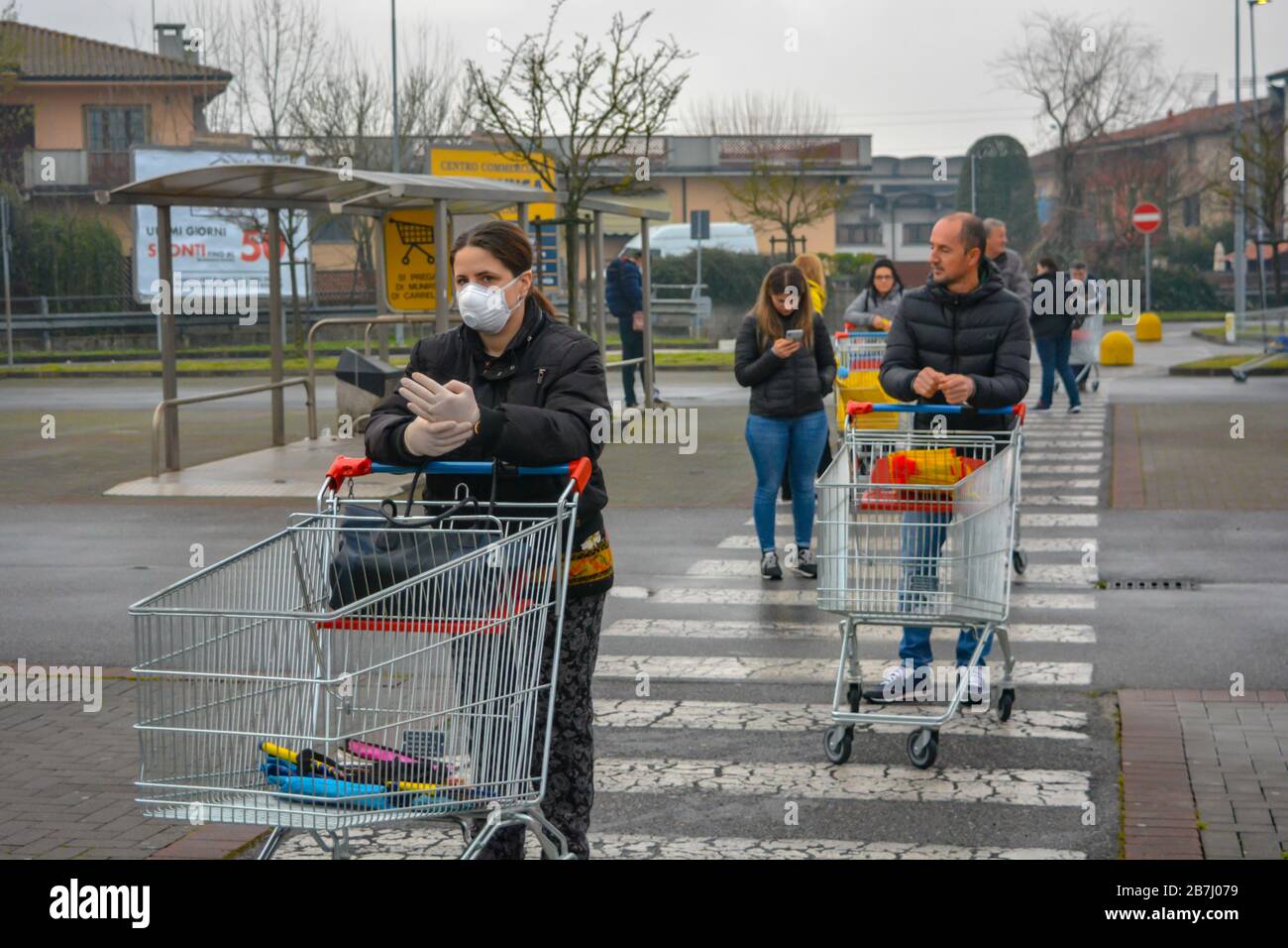 Closeup of a woman with mask and gloves standing with her shopping cart in line to stock up groceries. Fear for coronavirus pandemic, panic buying Stock Photo