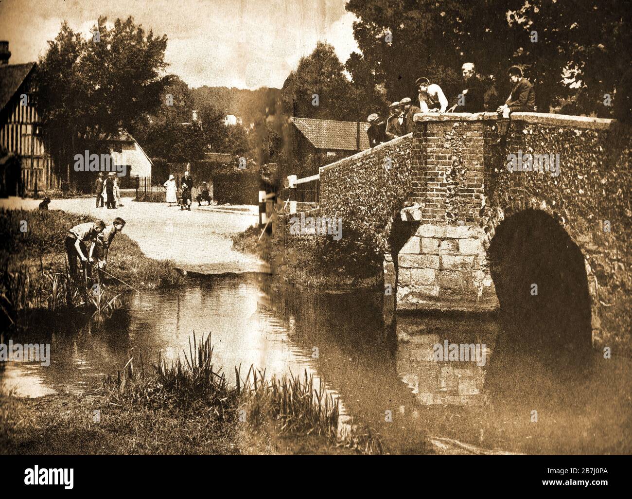 A vintage photograph of the ford at Eynsford bridge Kent in the 1940's. Schoolboys and old men stand on the bridge watching a father and son fishing in the quiet days when motor traffic was rarely seen. It has fatured over the years on TV  and in films , including a series of '20 Miles from Piccadilly Circus' featuring Alex Kennedy (Smithy), 'Save Lullingstone Castle' and a scene in the local church in 'Love Actually'.Eynsford was first documented in 864 and has three historical  sites, Lullingstone Castle, Eynsford Castle,  and a Roman villa Stock Photo