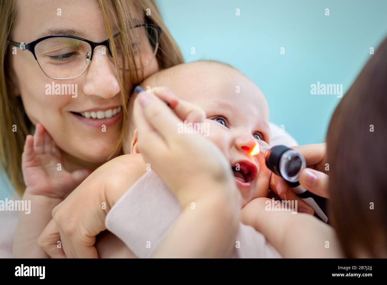Doctor pediatrist examining childs nose with otoscope. Mom holding baby