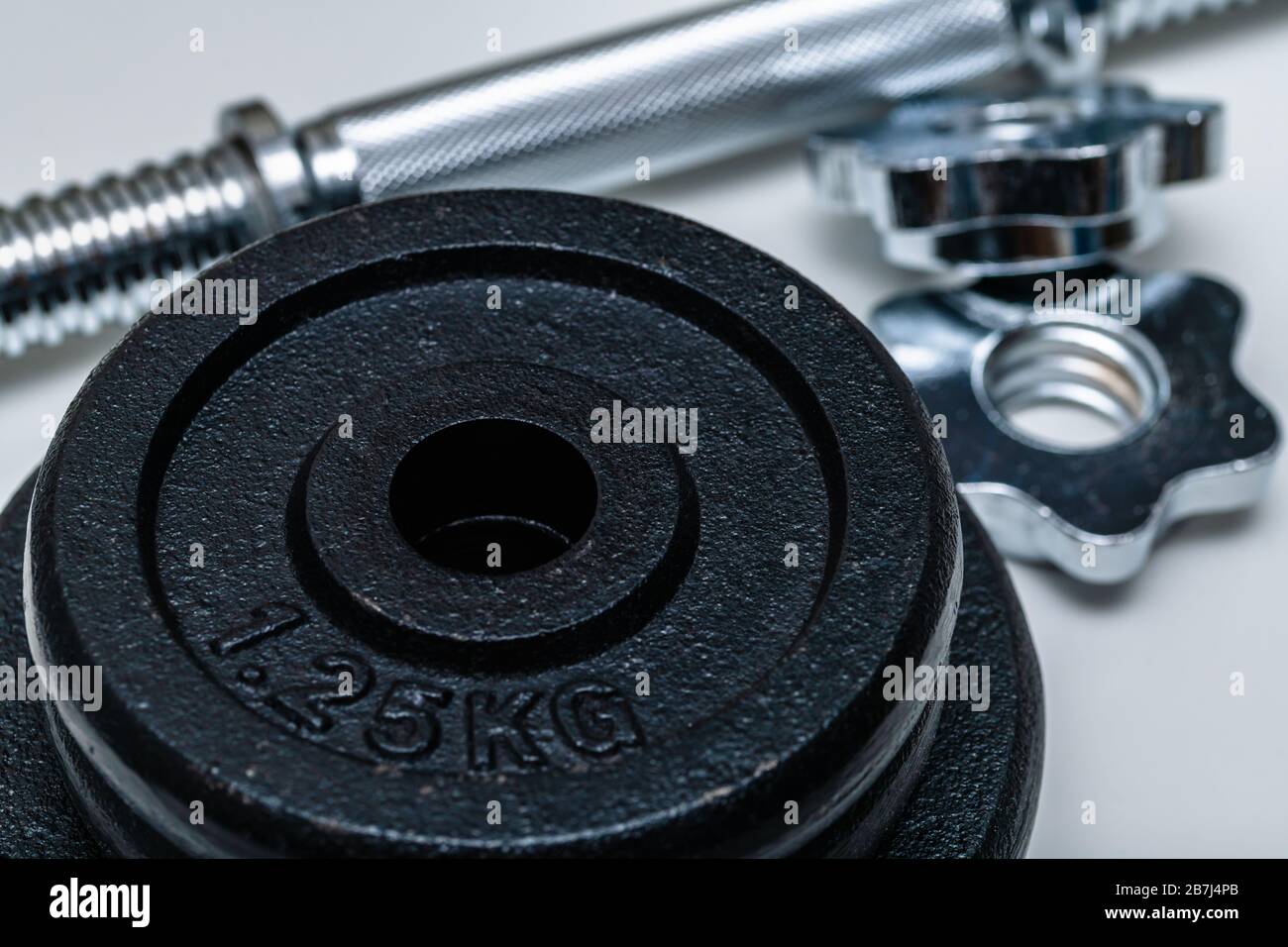 Close-up of four black weight training weights in focus stacked upon each other with handle and locks out of focus on a white background. Concept of t Stock Photo