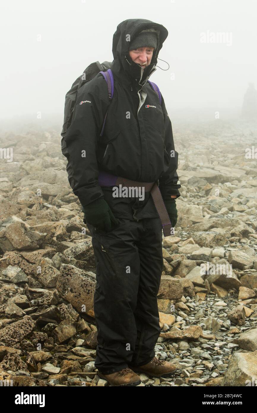 A well equipped walker on the icy cloud covered summit of Ben Nevis wearing  winter clothing and looking cold Stock Photo - Alamy
