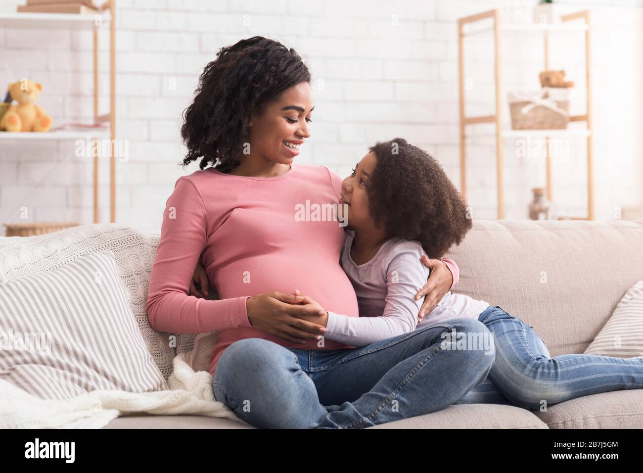 Cute little black girl and her pregnant mom embracing at home Stock Photo