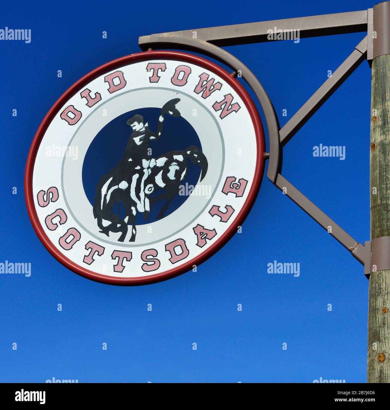 A round Old town Scottsdale sign in red and blue with a bucking bronco & cowboy clip art in center hangs from wooden post in Old town Scottsdale, AZ Stock Photo