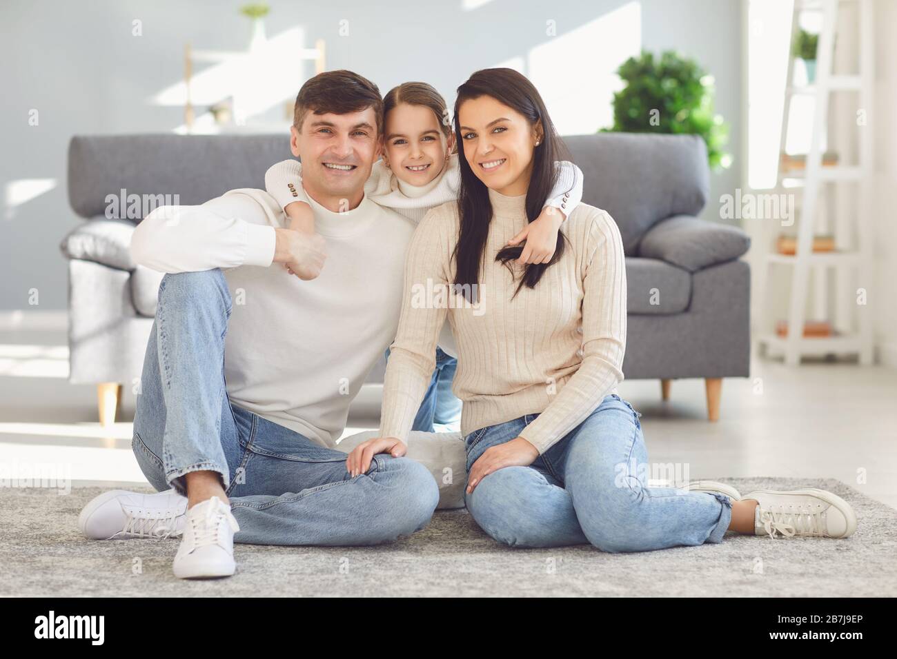 Happy smiling family hugging sitting on floor in room at home. Stock Photo