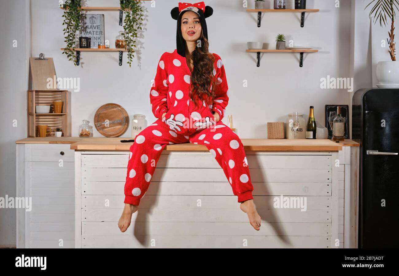 Maiden dressed up in red plush pajama in form of cartoon character mouse.  Having fun at bachelorette party sitting on kitchen table, showing tongue  Stock Photo - Alamy