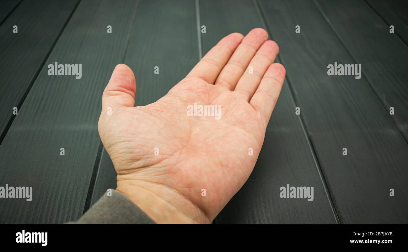 Front of a white adult man's hand outstretched on a gray wooden table Stock Photo