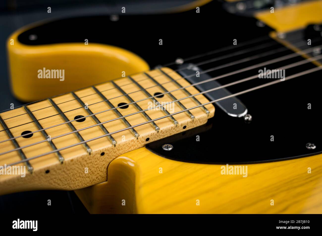 Electric guitar strings on neck and frets. American classic lacquered guitar in yellow tones. Stock Photo