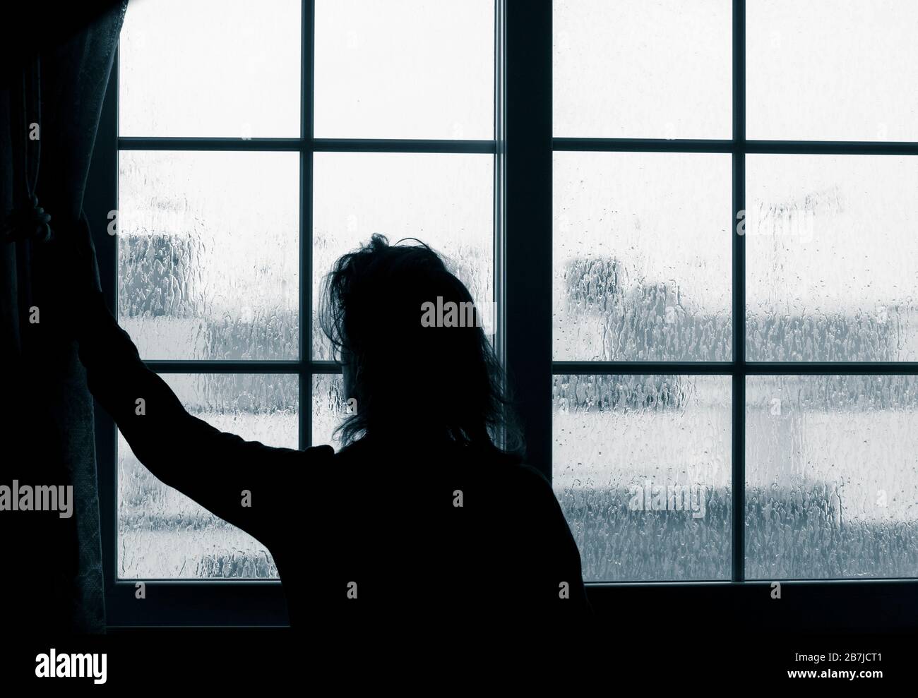 Woman looking out of window on rainy day. Conept image; female depression, domestic abuse, self isolation, quarantine, Coronavirus, Stock Photo