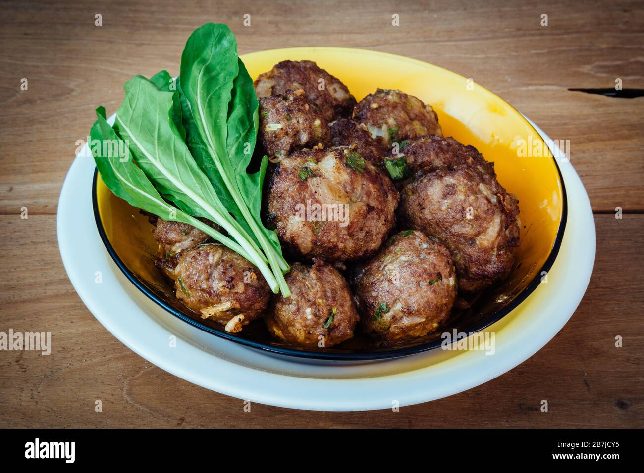 Beef meatballs and raw fresh arucula leaf vegetable, ready to eat, in plate on rustic wooden table Stock Photo