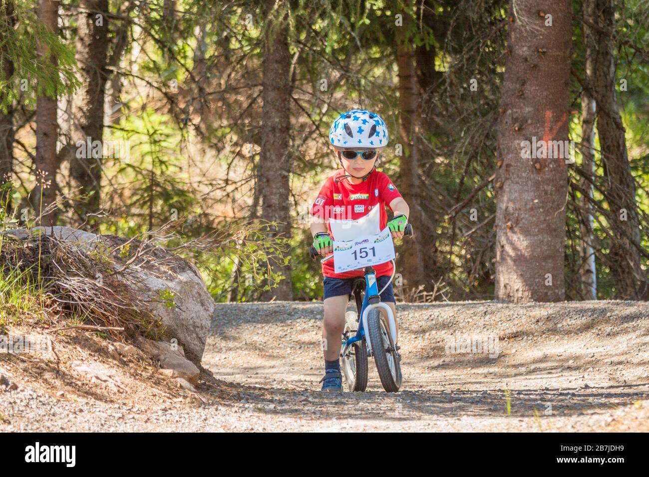 2-3 year old kid on kick-bike, with sunglasses and helmet, at a bike park pump track Stock Photo