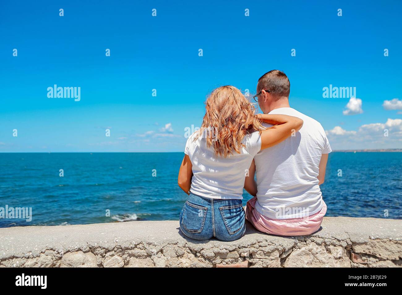 Content resting man and woman in sunglasses hugging with blue sea and ...