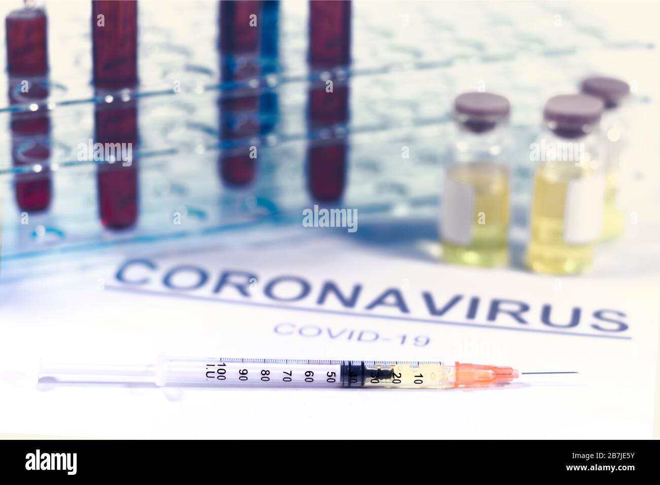 Syringe and vaccine vials with a test tube holder. Paper with the word coronavirus and covid-19. Virus, vaccine and treatment concepts Stock Photo