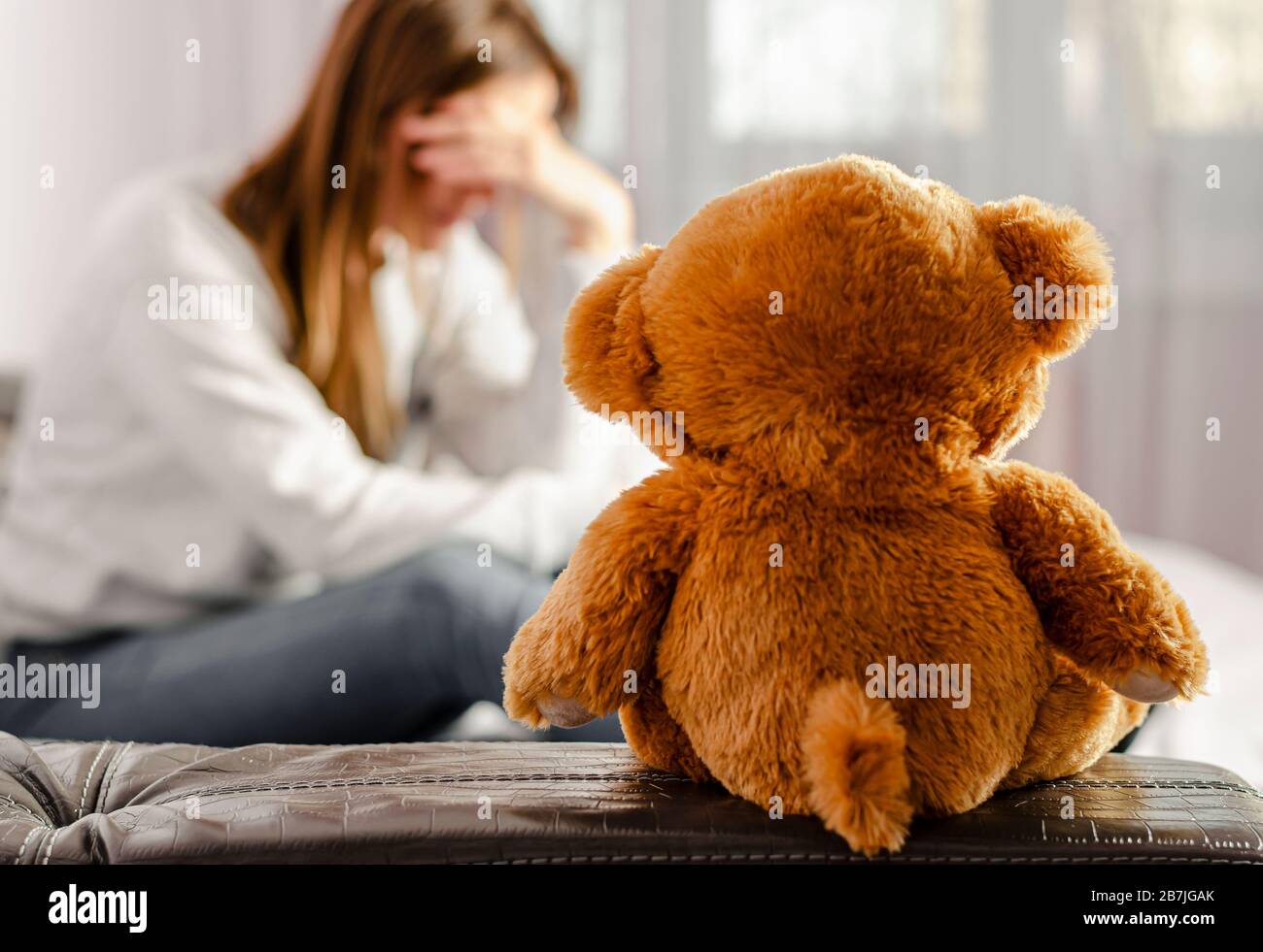 Selected focus on brown teddy bear sitting on depressed and pensive woman background. Infertility and divorce concept Stock Photo