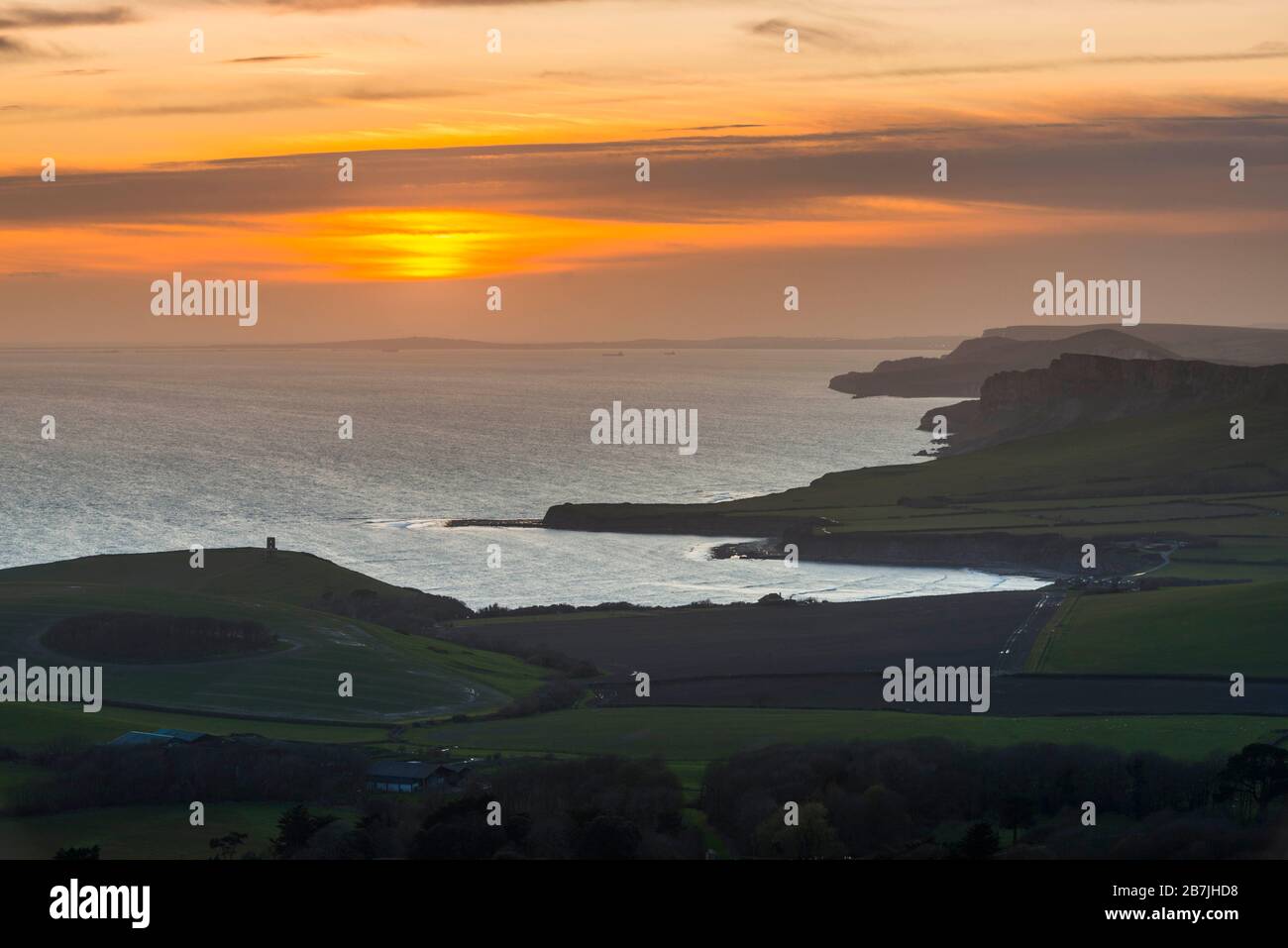 Kimmeridge, Dorset, UK.  16th March 2020.  UK Weather.   The sky glows orange at sunset viewed from Swyre Head near Kimmeridge on the Jurassic coast of Dorset looking west across Kimmeridge Bay and Warbarrow Bay after a day of warm sunshine and clear blue skies.  Picture Credit: Graham Hunt/Alamy Live News Stock Photo