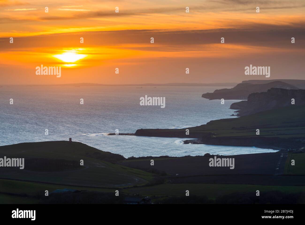 Kimmeridge, Dorset, UK.  16th March 2020.  UK Weather.   The sky glows orange at sunset viewed from Swyre Head near Kimmeridge on the Jurassic coast of Dorset looking west across Kimmeridge Bay and Warbarrow Bay after a day of warm sunshine and clear blue skies.  Picture Credit: Graham Hunt/Alamy Live News Stock Photo
