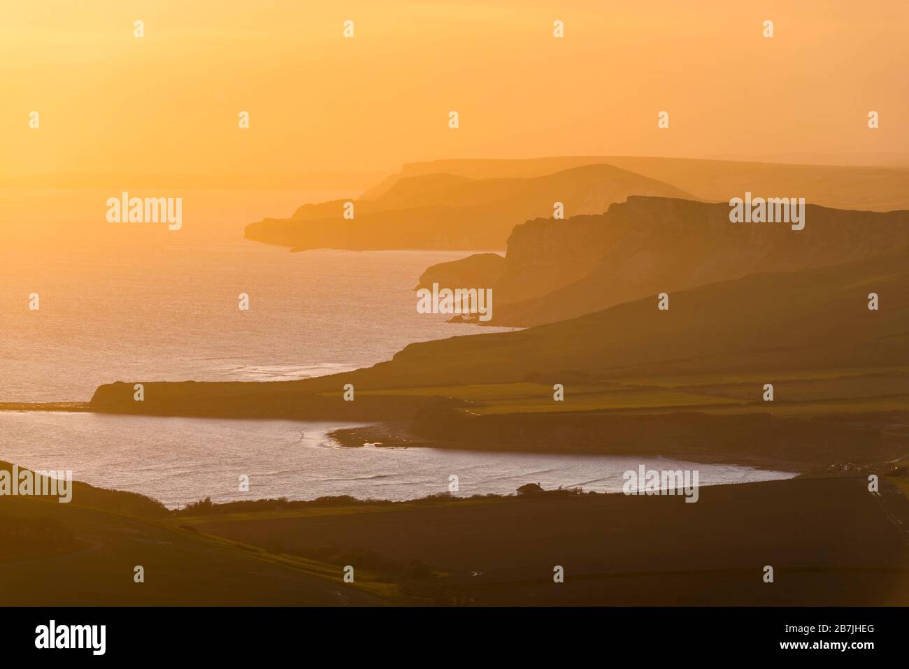 Kimmeridge, Dorset, UK.  16th March 2020.  UK Weather.   The sky glows orange at sunset viewed from Swyre Head near Kimmeridge on the Jurassic coast of Dorset looking west across Kimmeridge Bay and Warbarrow Bay after a day of warm sunshine and clear blue skies.  Picture Credit: Graham Hunt/Alamy Live News Stock Photo