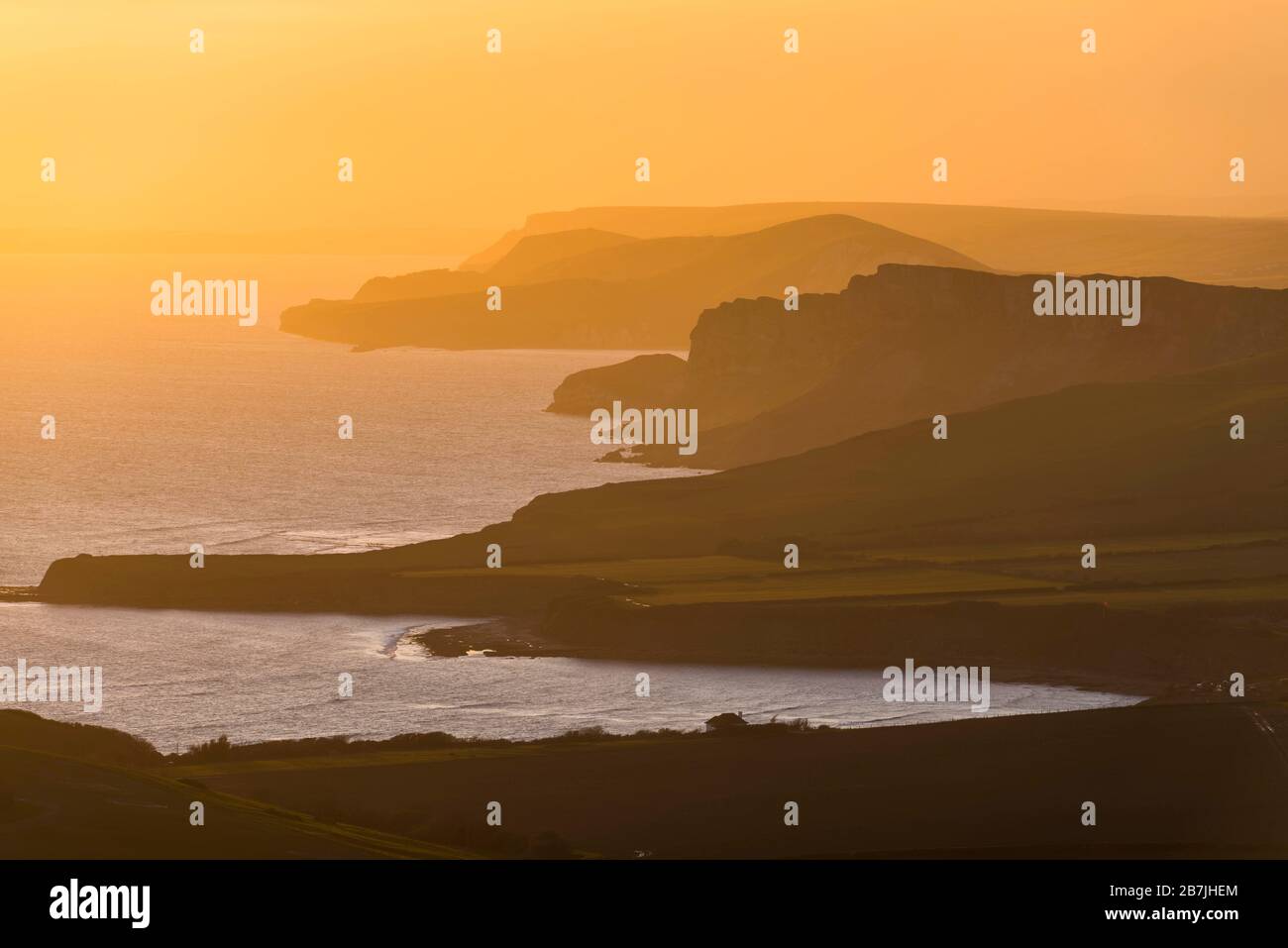 Kimmeridge, Dorset, UK.  16th March 2020.  UK Weather.   The sky glows orange at sunset viewed from Swyre Head near Kimmeridge on the Jurassic coast of Dorset looking west across Kimmeridge Bay and Warbarrow Bay after a day of warm sunshine and clear blue skies.  Picture Credit: Graham Hunt/Alamy Live News Stock Photo