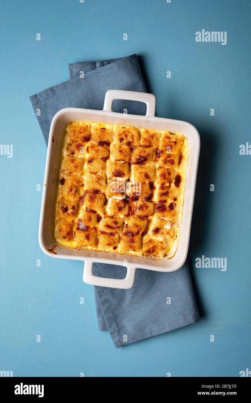 Cheese gnocchi in a white tray on a blue table. Italian traditional recipe with roasted gnocchi. Stock Photo