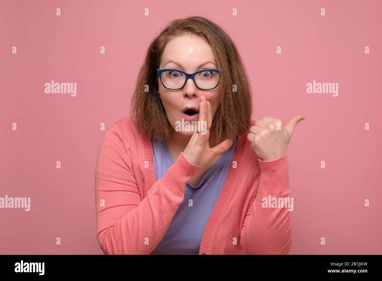 Caucasian young woman in glasses telling a secret against a pink background Stock Photo