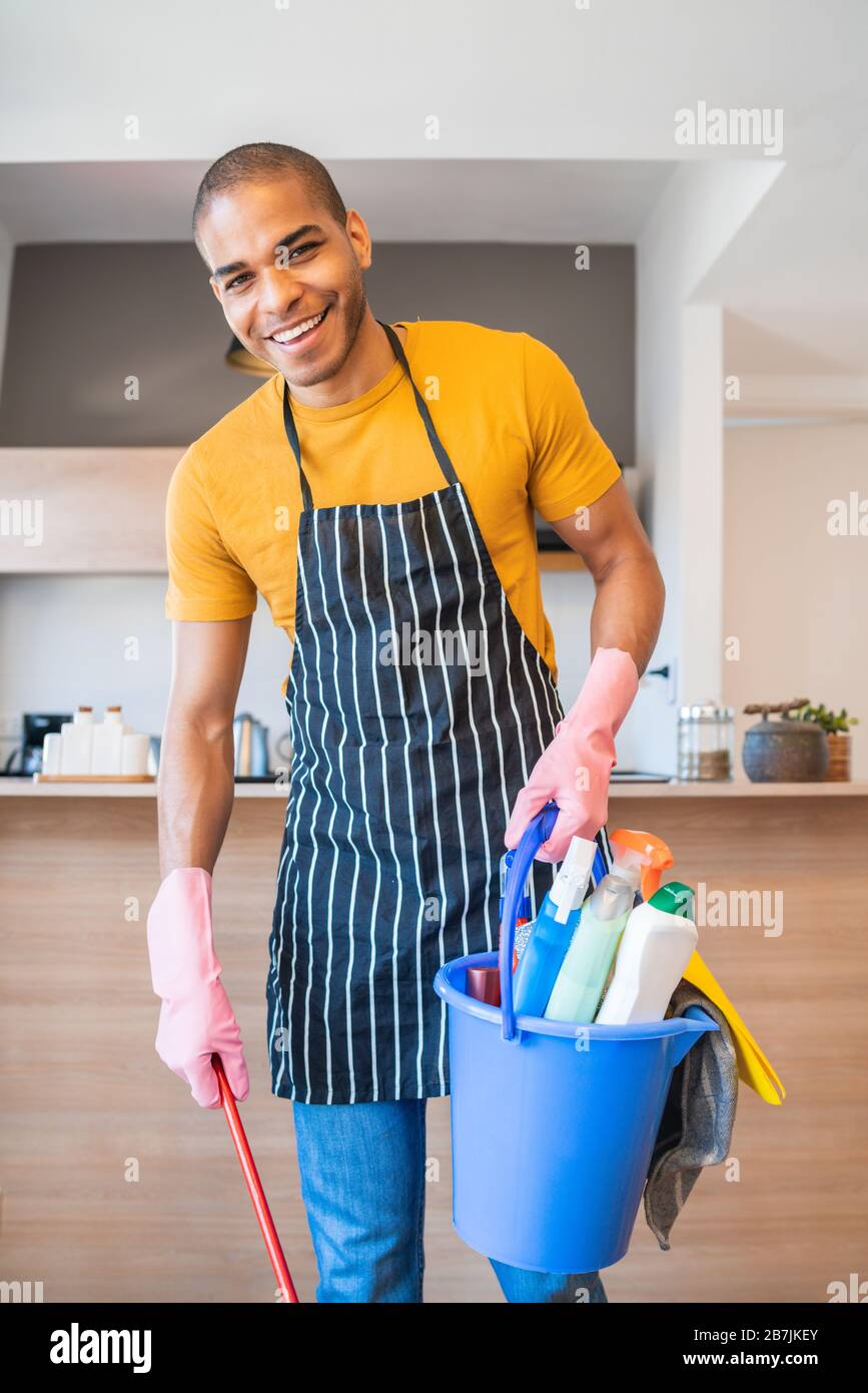 Portrait of young latin man holding a bucket with cleaning items at home. Housekeeping and