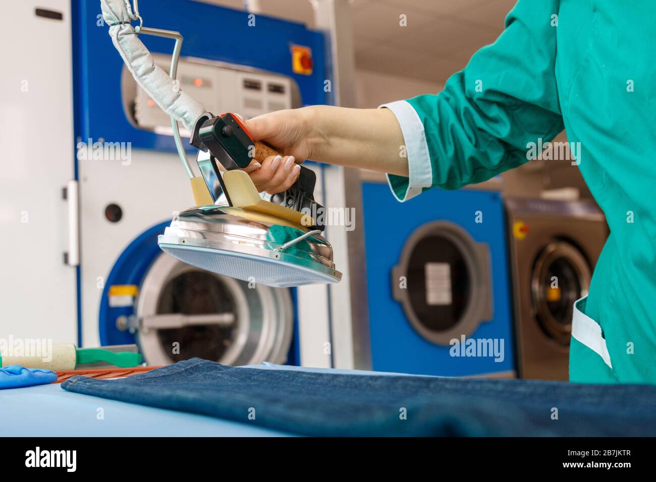 Female hand ironing blue jeans in a dry cleaning laundry service Stock Photo